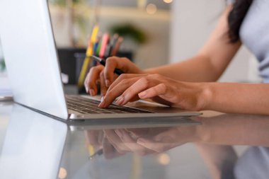 Genç bir kadın işyerinde özenle oturuyor, kendini online iş işine kaptırmış ve güvenilir dizüstü bilgisayarıyla planlar ve geliştirme stratejileri için kendini daktilo ve araştırma yapmaya adamış..