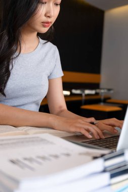 Genç bir kadın işyerinde özenle oturuyor, kendini online iş işine kaptırmış ve güvenilir dizüstü bilgisayarıyla planlar ve geliştirme stratejileri için kendini daktilo ve araştırma yapmaya adamış..