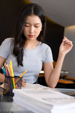 Genç bir kadın ya da iş kadını modern bir çalışma alanında özenle oturuyor, güvenilir laptopuyla çalışmaya dalmış ve yararlı bilgilerle zihnini zenginleştirmek için kitap okumaya kendini adamış..