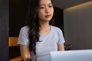 Genç bir kadın işyerinde özenle oturuyor, kendini online iş işine kaptırmış ve güvenilir dizüstü bilgisayarıyla planlar ve geliştirme stratejileri için kendini daktilo ve araştırma yapmaya adamış..