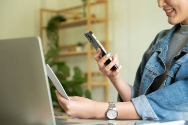 Genç bayan mimar ya da iç mimar elinde akıllı telefonuyla ofisindeki masasında oturuyor, bunu internet bilgilerini araştırmak, müşterilerle sohbet etmek ve renkli panellerin fotoğraflarını çekmek için kullanıyor.. 