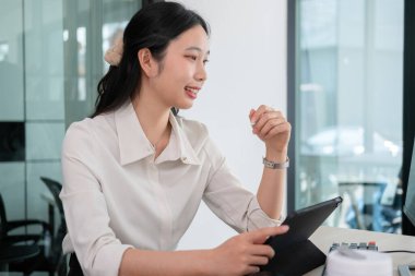 Etrafı bilgisayar ve iPad ile çevrili genç bir kadın çalışma masasında çalışıyor. Akıllı kalem, veri ve potansiyel yatırım fırsatları eğilimi kullanarak bilgisayar ve tablet ekranında gösterilen hisse senedi grafiklerini inceliyor.