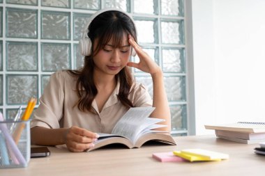 Genç bir kadın ya da öğrenci, elinde notlar ve kitaplarla çalışma alanında oturmuş, kulaklıkla müzik eşliğinde verimlilik ve rahatlama üzerine bir kitap okumaktan keyif alıyor..