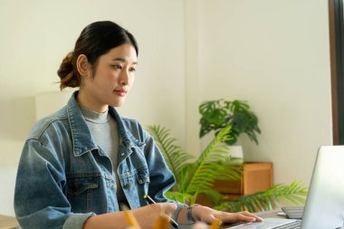 Genç bayan mimar veya iç mimar, elinde tabletle ofisinde masasında oturuyor, dizüstü bilgisayardaki tasarım fikirlerini çiziyor ve hayata geçiriyor ve çizelgelerden renkler seçiyor, tüm projeyi öngörüyor.. 