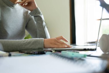 Genç bayan mimar ya da iç mimar ofisinde ekipmanlarla masasında oturuyor, dizüstü bilgisayarla çalışıyor ve tasarım fikirlerini hayata geçiriyor ve çizelgelerden renkler seçiyor, tüm projeyi hayal ederek. 