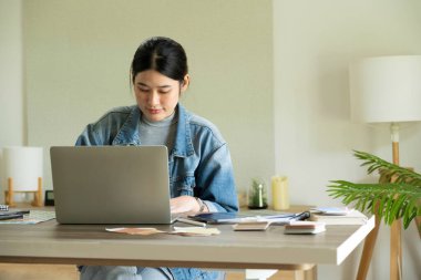 Genç bayan mimar ya da iç mimar ofisinde ekipmanlarla masasında oturuyor, dizüstü bilgisayarla çalışıyor ve tasarım fikirlerini hayata geçiriyor ve tüm projeyi öngören çizelgelerden renkleri seçiyor.. 