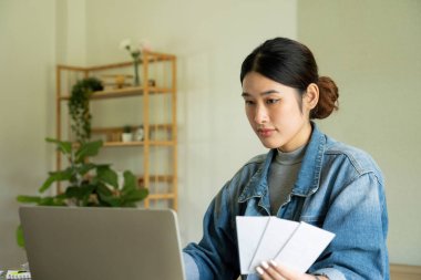 Genç bayan mimar veya iç mimar, elinde tabletle ofisinde masasında oturuyor, dizüstü bilgisayardaki tasarım fikirlerini çiziyor ve hayata geçiriyor ve çizelgelerden renkler seçiyor, tüm projeyi öngörüyor.. 