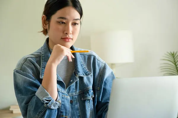 stock image Young female architect or interior designer sits at her desk in the office, she works with laptop and brings her design ideas to life and selects colors from charts, envisioning and thinking the entire project while holding a pencil. 