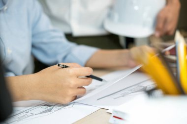 İki kadın ve erkek mühendis veya mimar çalışma masasında inşaat modeli ve ofis işyerindeki diğer ekipmanlarla birlikte çalışıyor. Erkek bir iş arkadaşı konuşurken inşaat projesinin planlarını, planlarını ve planlarını ele alıyor ve tartışıyorlar.