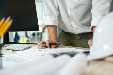 İki erkek ve kadın mühendis ya da mimar çalışma masasında profesyonel ekipmanlarla birlikte çalışarak inşaat projesinin planlarını gösteriyorlar, çiziyorlar, planlıyorlar ve tartışıyorlar..