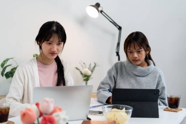 Evde dizüstü bilgisayar kullanan ve kitap okuyan kız öğrenci, İnternet üzerinden öğrenim.
