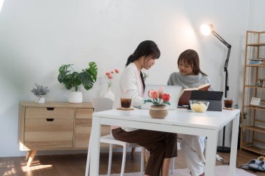 Evde dizüstü bilgisayar kullanan ve kitap okuyan kız öğrenci, İnternet üzerinden öğrenim.