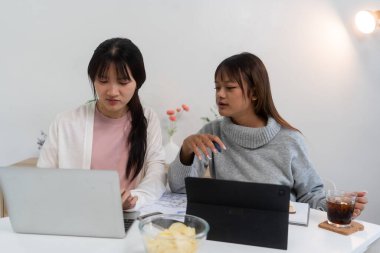 Evde dizüstü bilgisayar kullanan ve kitap okuyan kız öğrenci, İnternet üzerinden öğrenim.