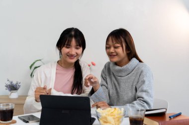 Evde dizüstü bilgisayar kullanan ve kitap okuyan kız öğrenci, İnternet üzerinden öğrenim.