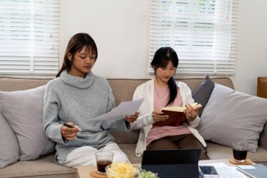 Evde dizüstü bilgisayar kullanan ve kitap okuyan kız öğrenci, İnternet üzerinden öğrenim.