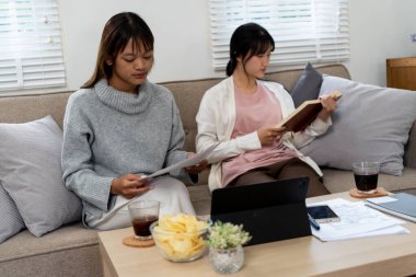 Evde dizüstü bilgisayar kullanan ve kitap okuyan kız öğrenci, İnternet üzerinden öğrenim.