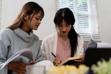 Evde dizüstü bilgisayar kullanan ve kitap okuyan kız öğrenci, İnternet üzerinden öğrenim.