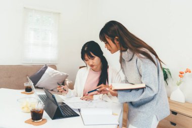 Evde dizüstü bilgisayar kullanan ve kitap okuyan kız öğrenci, İnternet üzerinden öğrenim.