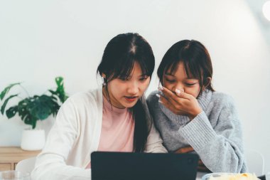 Evde dizüstü bilgisayar kullanan ve kitap okuyan kız öğrenci, İnternet üzerinden öğrenim.