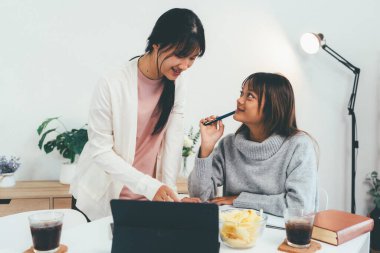Evde dizüstü bilgisayar kullanan ve kitap okuyan kız öğrenci, İnternet üzerinden öğrenim.