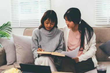 Evde dizüstü bilgisayar kullanan ve kitap okuyan kız öğrenci, İnternet üzerinden öğrenim.