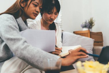 Evde dizüstü bilgisayar kullanan ve kitap okuyan kız öğrenci, İnternet üzerinden öğrenim.