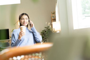 Genç Asyalı kadın pencerenin yanında kitap okuyarak huzurlu bir anın tadını çıkarıyor. Sakin yaşam tarzı, kendi kendine öğrenme ve evdeki farkındalık..