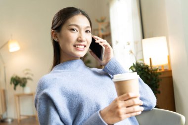 Genç Asyalı kadın pencerenin yanında kitap okuyarak huzurlu bir anın tadını çıkarıyor. Sakin yaşam tarzı, kendi kendine öğrenme ve evdeki farkındalık..