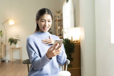 Genç Asyalı kadın pencerenin yanında kitap okuyarak huzurlu bir anın tadını çıkarıyor. Sakin yaşam tarzı, kendi kendine öğrenme ve evdeki farkındalık..