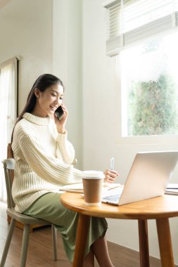Genç Asyalı kadın pencerenin yanında kitap okuyarak huzurlu bir anın tadını çıkarıyor. Sakin yaşam tarzı, kendi kendine öğrenme ve evdeki farkındalık..