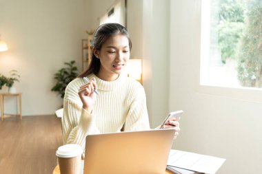 Genç Asyalı kadın pencerenin yanında kitap okuyarak huzurlu bir anın tadını çıkarıyor. Sakin yaşam tarzı, kendi kendine öğrenme ve evdeki farkındalık..