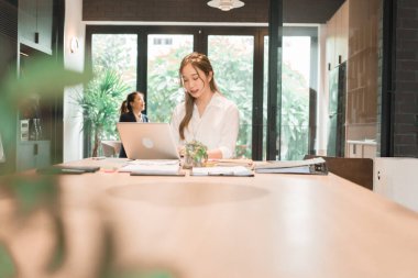 Üç genç iş kadınından oluşan bir grup, belgeler, tablet, dizüstü bilgisayar ve diğer ekipmanlarla birlikte bir masada oturuyorlar. Şirketi geliştirmek için bir tartışma ve planlama oturumu yapıyorlar..