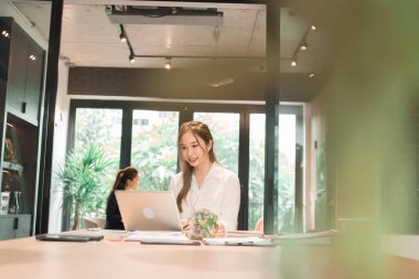 Üç genç iş kadınından oluşan bir grup, belgeler, tablet, dizüstü bilgisayar ve diğer ekipmanlarla birlikte bir masada oturuyorlar. Şirketi geliştirmek için bir tartışma ve planlama oturumu yapıyorlar..