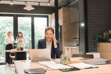 Üç genç iş kadınından oluşan bir grup, belgeler, tablet, dizüstü bilgisayar ve diğer ekipmanlarla birlikte bir masada oturuyorlar. Şirketi geliştirmek için bir tartışma ve planlama oturumu yapıyorlar..