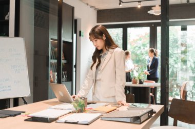 Üç genç iş kadınından oluşan bir grup, belgeler, tablet, dizüstü bilgisayar ve diğer ekipmanlarla birlikte bir masada oturuyorlar. Şirketi geliştirmek için bir tartışma ve planlama oturumu yapıyorlar..