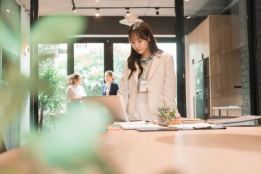 Üç genç iş kadınından oluşan bir grup, belgeler, tablet, dizüstü bilgisayar ve diğer ekipmanlarla birlikte bir masada oturuyorlar. Şirketi geliştirmek için bir tartışma ve planlama oturumu yapıyorlar..