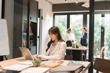 Üç genç iş kadınından oluşan bir grup, belgeler, tablet, dizüstü bilgisayar ve diğer ekipmanlarla birlikte bir masada oturuyorlar. Şirketi geliştirmek için bir tartışma ve planlama oturumu yapıyorlar..