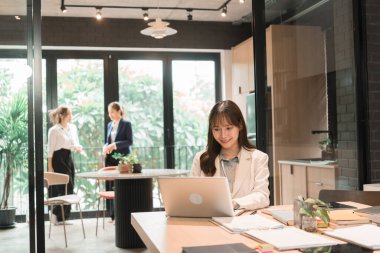 Üç genç iş kadınından oluşan bir grup, belgeler, tablet, dizüstü bilgisayar ve diğer ekipmanlarla birlikte bir masada oturuyorlar. Şirketi geliştirmek için bir tartışma ve planlama oturumu yapıyorlar..