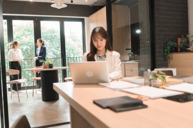 Üç genç iş kadınından oluşan bir grup, belgeler, tablet, dizüstü bilgisayar ve diğer ekipmanlarla birlikte bir masada oturuyorlar. Şirketi geliştirmek için bir tartışma ve planlama oturumu yapıyorlar..