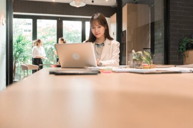 Üç genç iş kadınından oluşan bir grup, belgeler, tablet, dizüstü bilgisayar ve diğer ekipmanlarla birlikte bir masada oturuyorlar. Şirketi geliştirmek için bir tartışma ve planlama oturumu yapıyorlar..