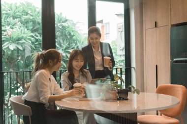 Üç genç iş kadınından oluşan bir grup, belgeler, tablet, dizüstü bilgisayar ve diğer ekipmanlarla birlikte bir masada oturuyorlar. Şirketi geliştirmek için bir tartışma ve planlama oturumu yapıyorlar..