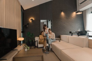 Üç genç Asyalı kadın evde bilgisayar ve kredi kartıyla online alışveriş yapıyor. Rahatlamış ve modern bir oturma odasında birlikte gülümsüyor ve eğleniyorlar..