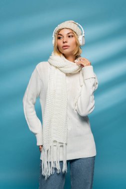 Sarışın, örgü şapkalı ve mavi kulaklıklı genç bir kadın. 