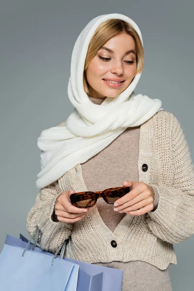 幸せな若いです女性で冬のスカーフ保持スタイリッシュなサングラスとショッピングバッグ絶縁上グレー — ストック写真
