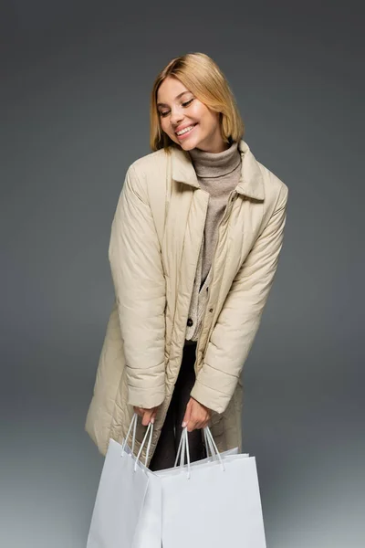 笑顔女性でベージュ冬ジャケット保持ショッピングバッグ孤立オングレー — ストック写真