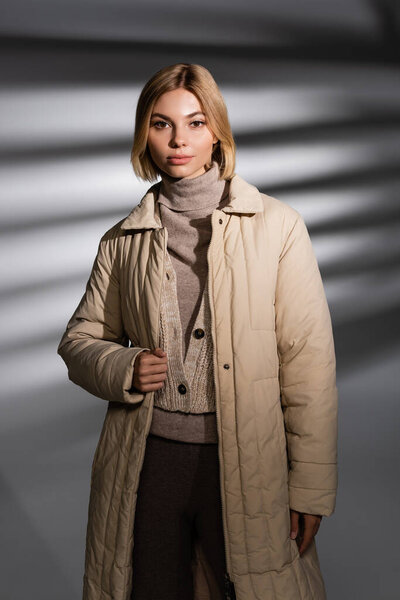 Pretty woman in beige winter outfit looking at camera on abstract grey background 