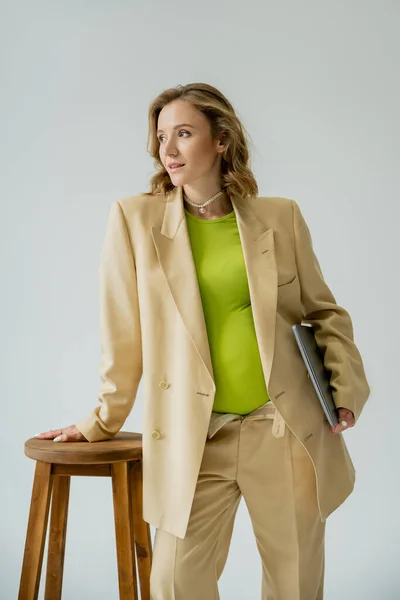 Takım Elbiseli Hamile Bir Kadın Dizüstü Bilgisayarını Gri Sandalyenin Yanında — Stok fotoğraf