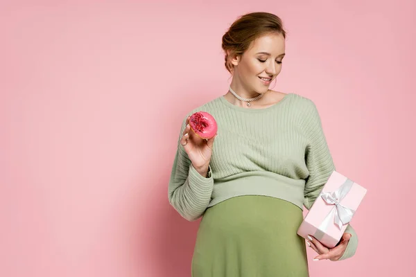 陽気妊娠中の女性保持甘いドーナツとギフト上のピンクの背景 — ストック写真
