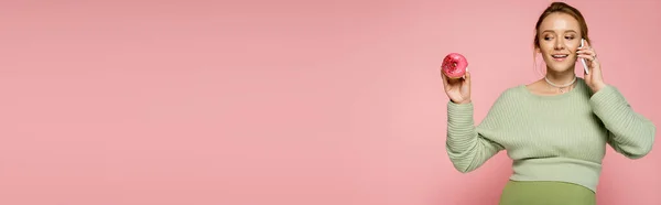 Щаслива Вагітна Жінка Говорить Смартфоні Дивиться Солодкий Пончик Ізольовано Рожевому — стокове фото