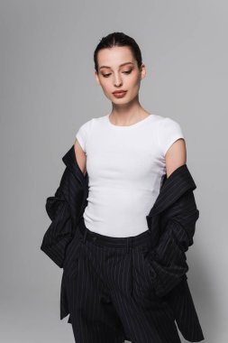 Tişörtlü ve siyah takım elbiseli moda kadın gri arka planda el ele tutuşuyor. 